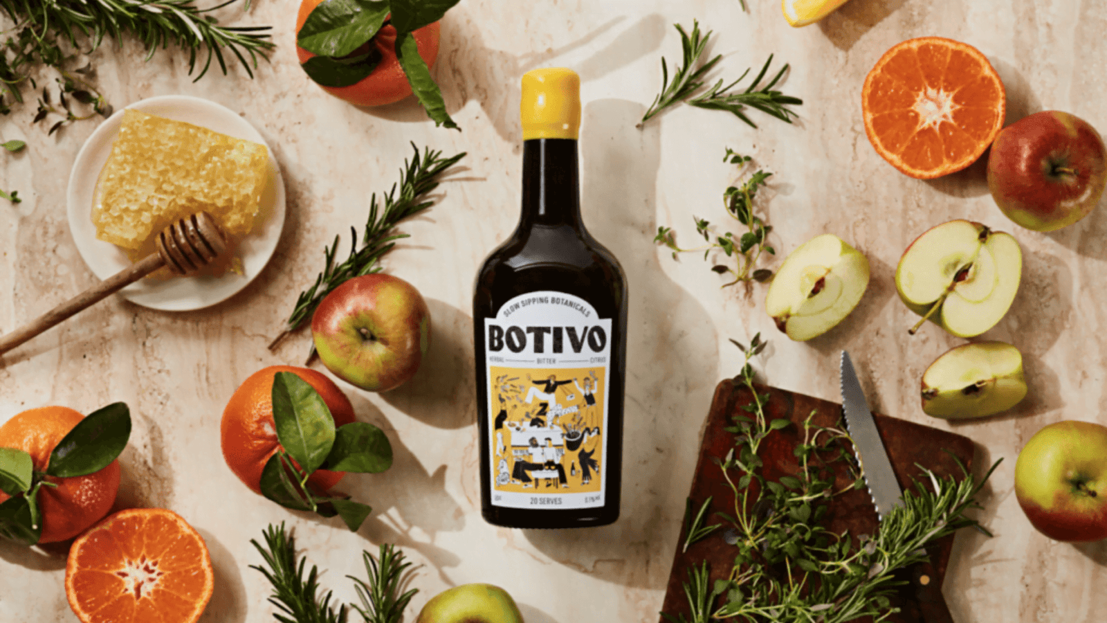 Fles Botivo, alcoholvrije spirit. Op tafel naast appels, honing, sinaasappels en rozemarijn.