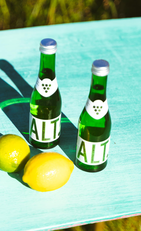 Twee flessen ALT Blanc de Blancs non-alcoholisch op een zomerse tafel naast verse citroenen.