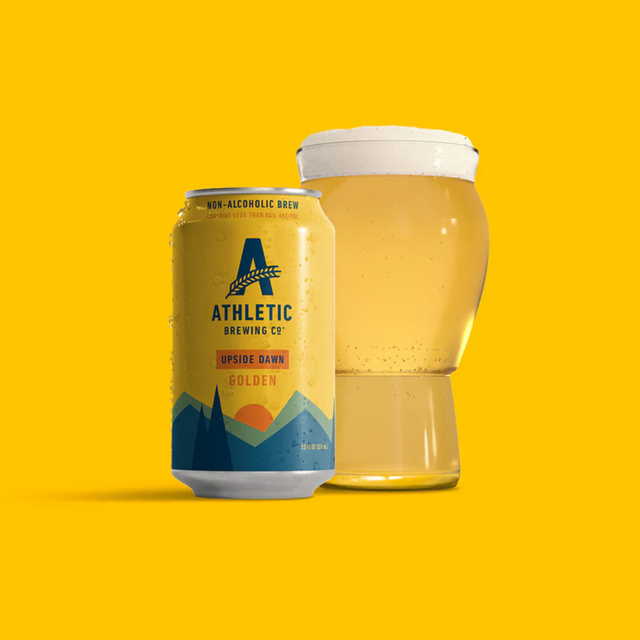Een glas gevuld met bier naast een blikje Athletic Brewing's Golden Ale op een gele achtergrond.