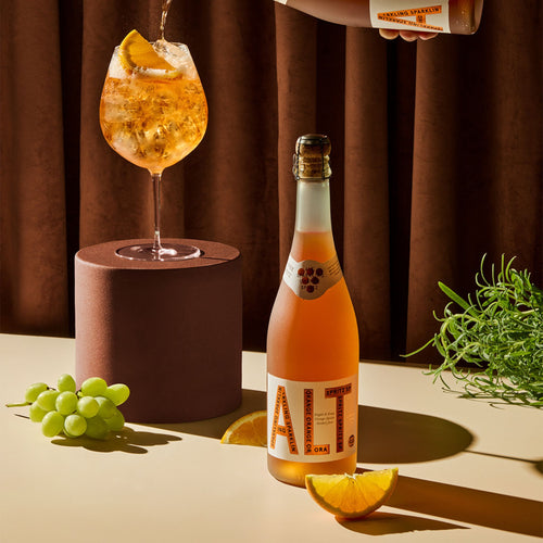 Fles alcoholvrije spritz met glas, sinaasappel, druiven en kruiden op tafel bij World of NIX