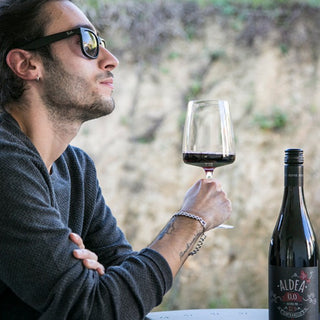 Man genietend van Aldea Tempranillo rode wijn in een glas, buiten met een natuurlijke achtergrond.