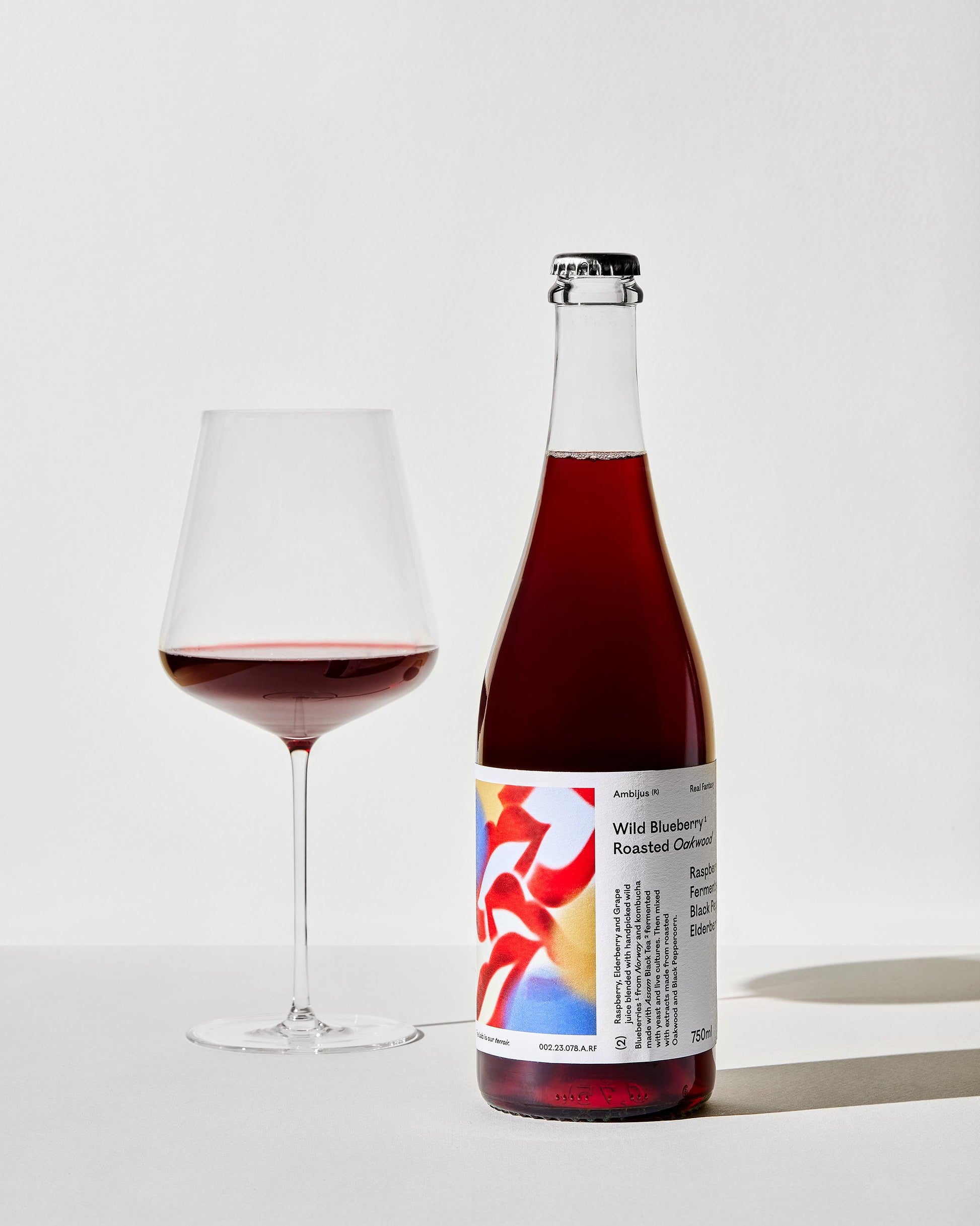 Een fles Ambijus met een gevuld glas en een witte achtergrond. 