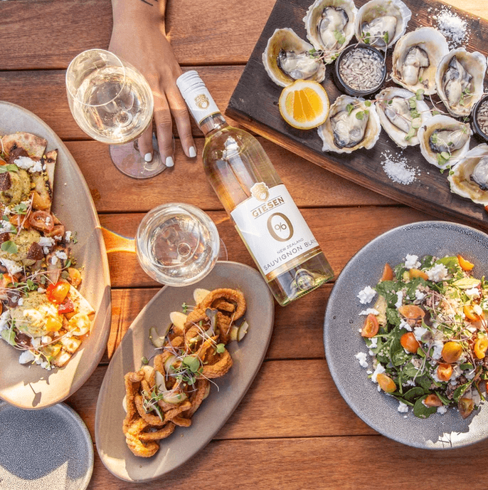 Giesen alcoholvrije Sauvignon Blanc op houten tafel met zeevruchten, salade en borrelhapjes