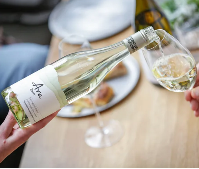 Een fles Ara alcoholvrije witte wijn die een glas inschenkt.