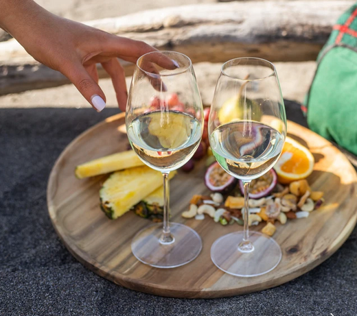 Een houten plank met een fles Ara Zero, omringd door glazen gevuld met witte wijn.